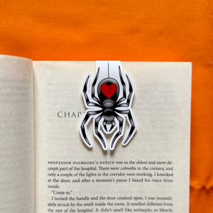 Spider with red heart magnetic bookmark on a page of an open book against an orange fabric background