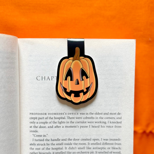 Open book with a Halloween jack o' lantern bookmark on an orange background