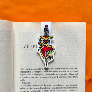 Open book with a dagger in heart magnetic bookmark on an orange fabric background