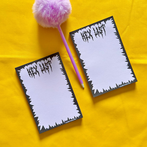 Two notepads with a pink pom-pom and pencil on a yellow surface.