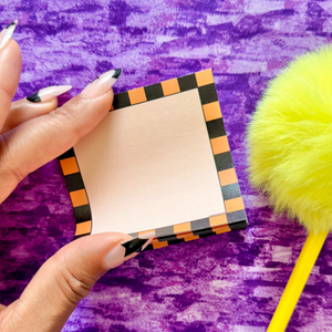 Hand holding a small square sticky notepad with a colorful border on a purple textured background