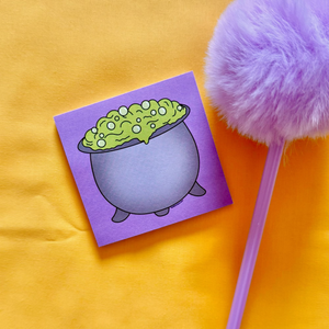 Sticky notepad with a cauldron design with purple background. A pen with fluffy top placed next to it.